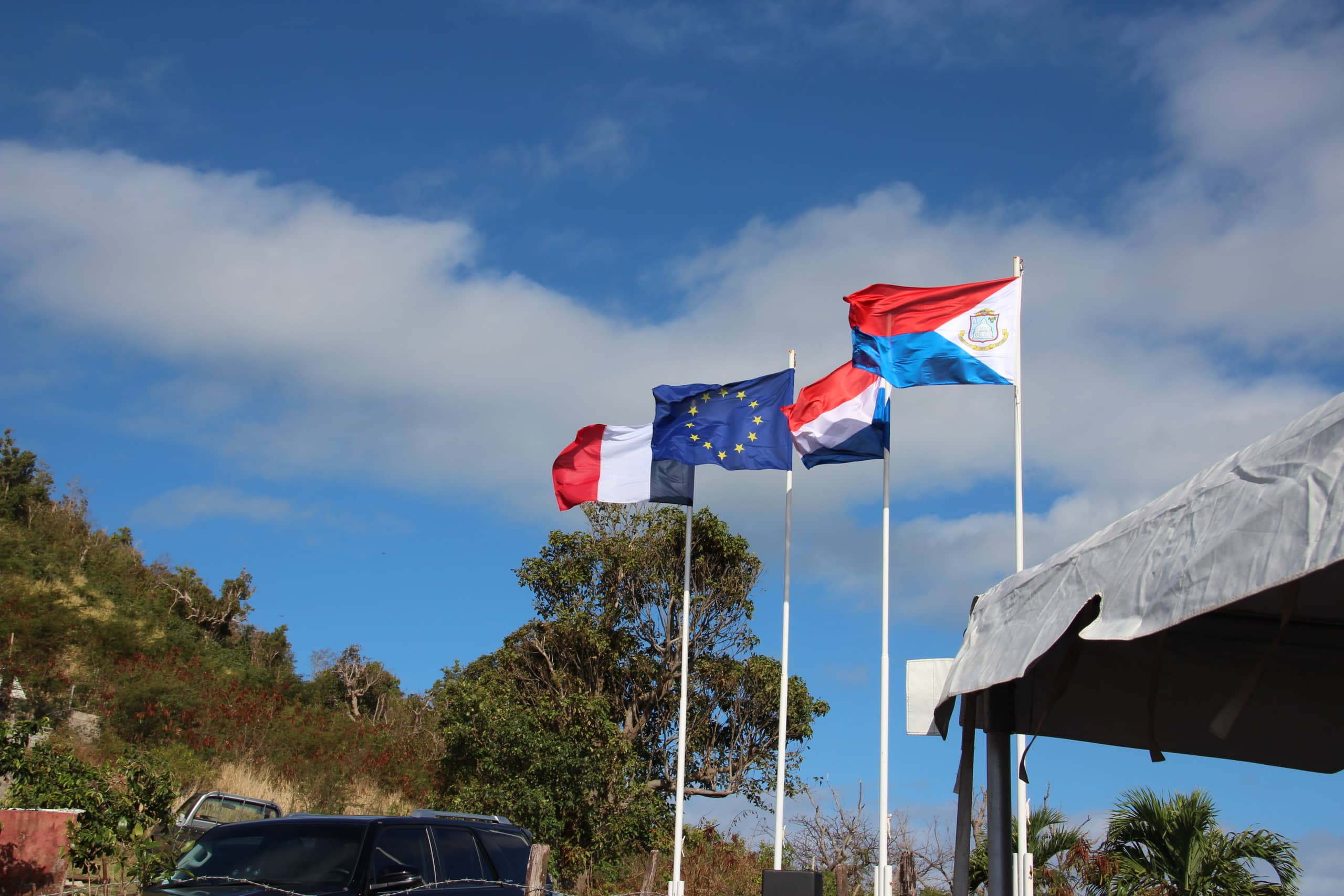 Vier vlaggen staan naast elkaar: de vlaggen van Frankrijk, de EU, Nederland en Sint Maarten.