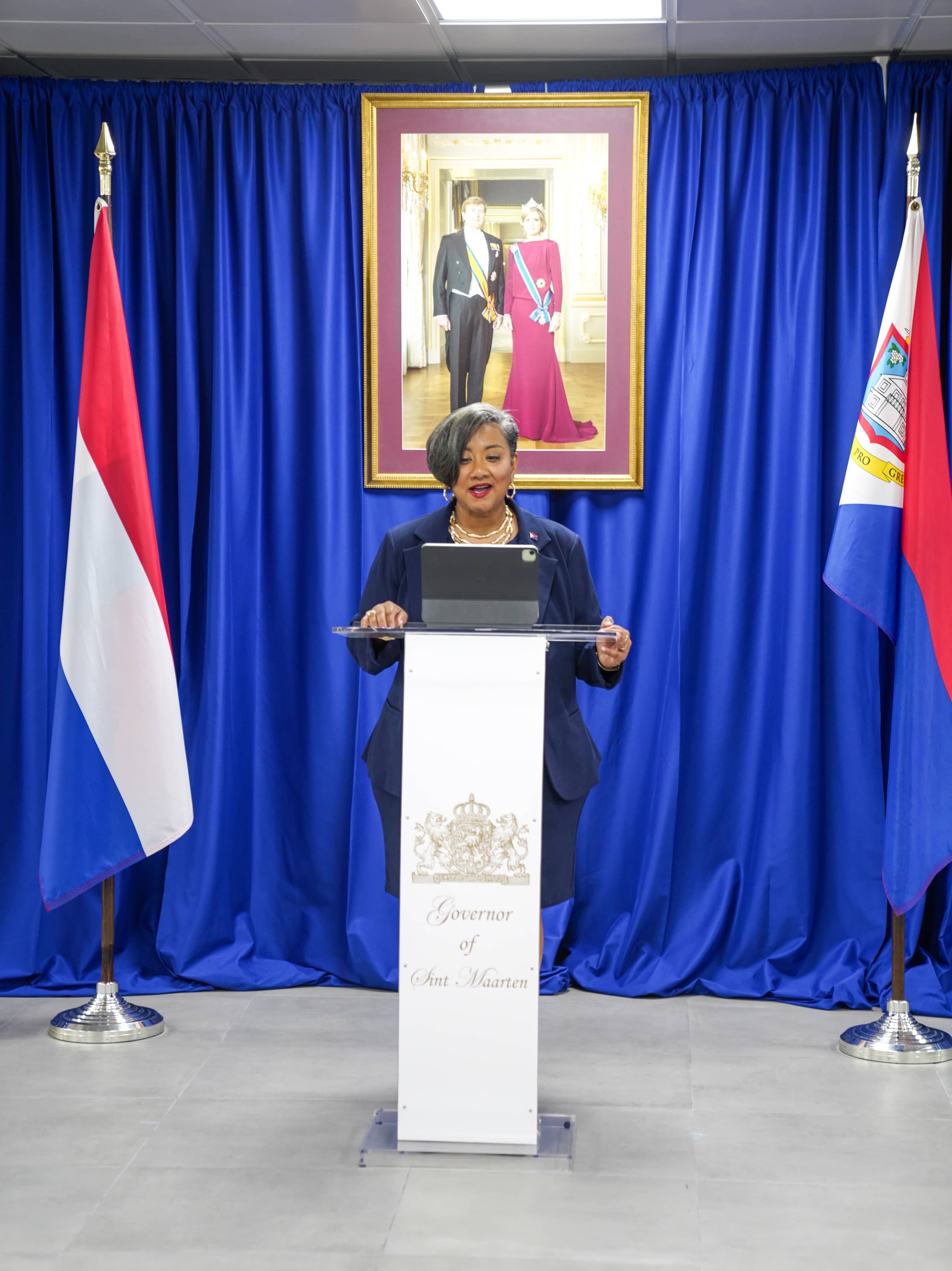 Waarnemend Gouverneur Bird-Lake houdt haar toespraak. Op de achtergrond het Staatsieportret van Koning Willem-Alexander en Koningin Maxima. Links achter de Waarnemend Gouverneur staat de Nederlandse vlag. Rechts achter, de Sint Maartense vlag.
